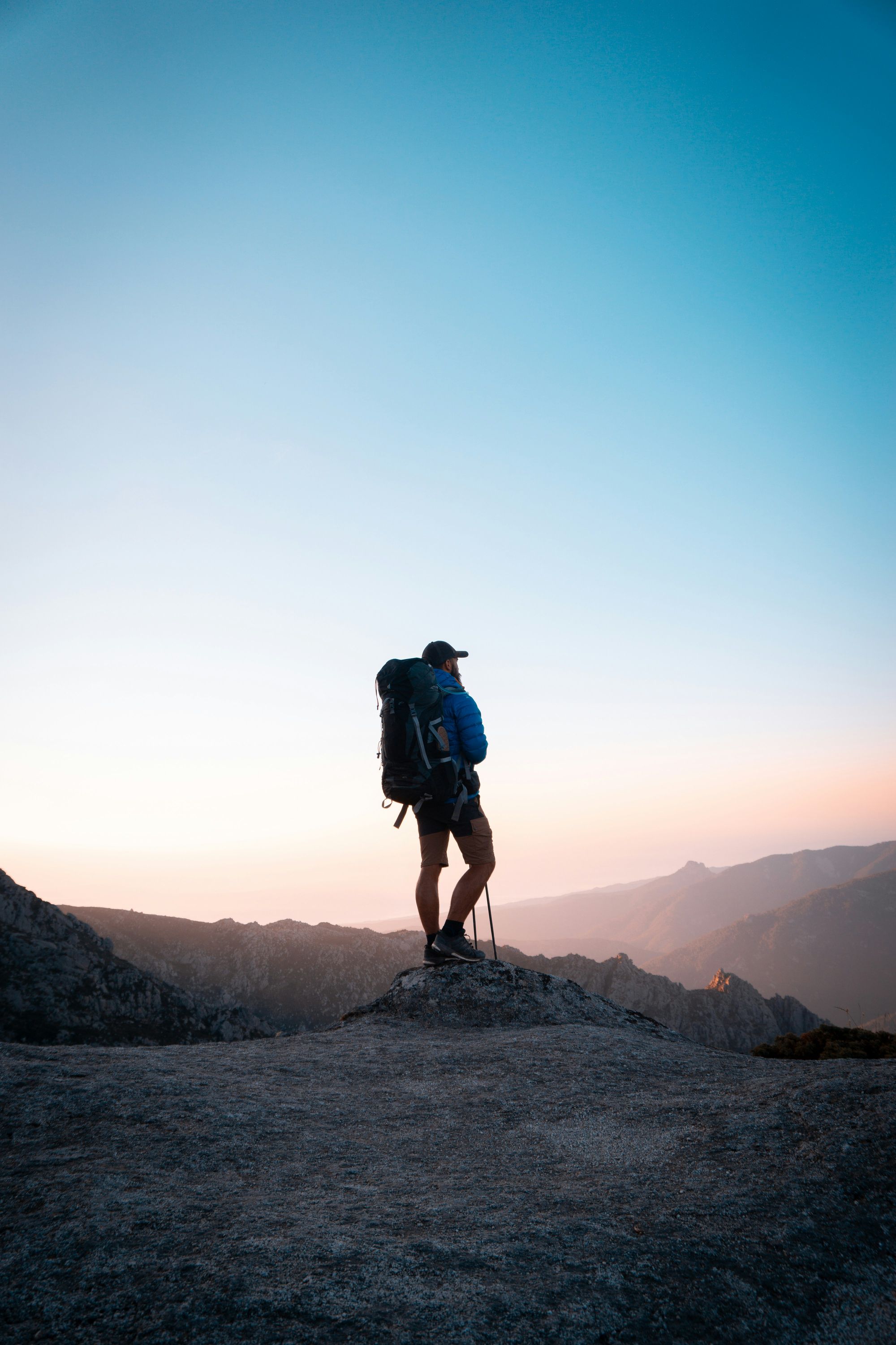 Wanderer mit Rucksack steht bei Sonnenuntergang auf einem Felsen über den Bergen